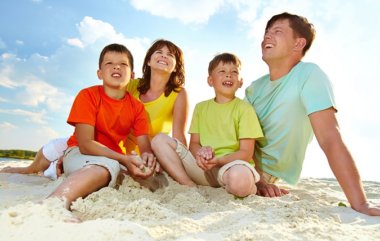 Photo of happy family sitting on sand during summer rest