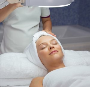 Portrait of happy young woman lying down, keeping her eyes closed, relaxing after facial treatment in spa salon