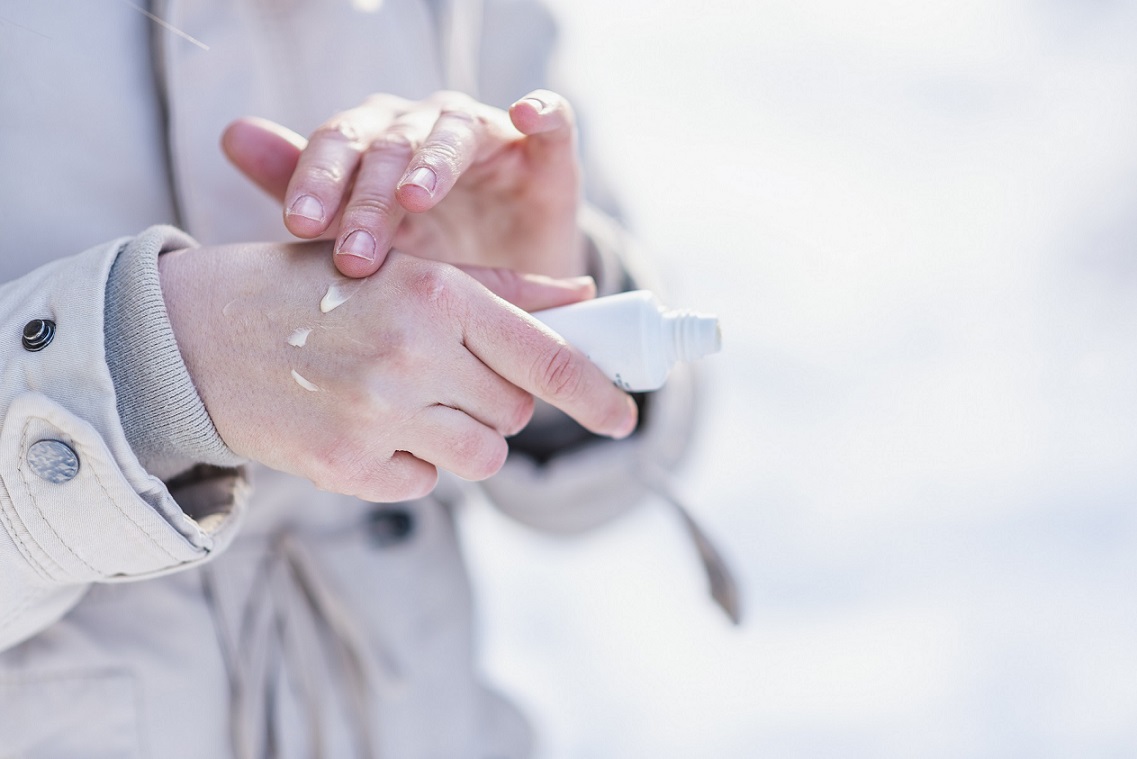 Front view portrait of a woman applying moisturizer cream to hydrate hands with a snowy mountain in the background. Woman use hand cream on dry hand